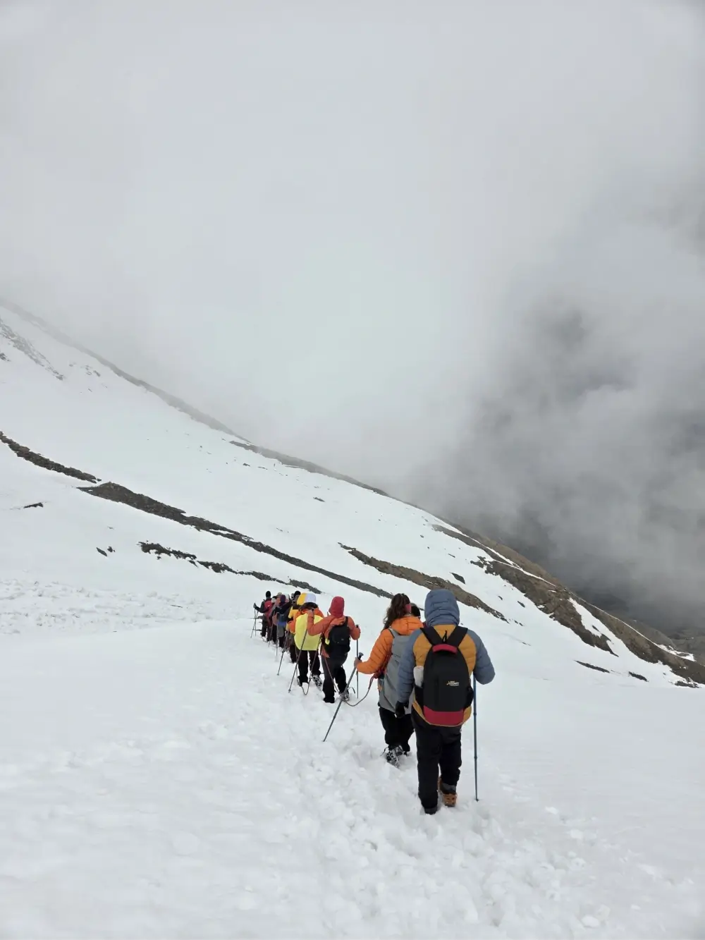 Trekkers crossing a snow-covered trail on the Roopkund Trek